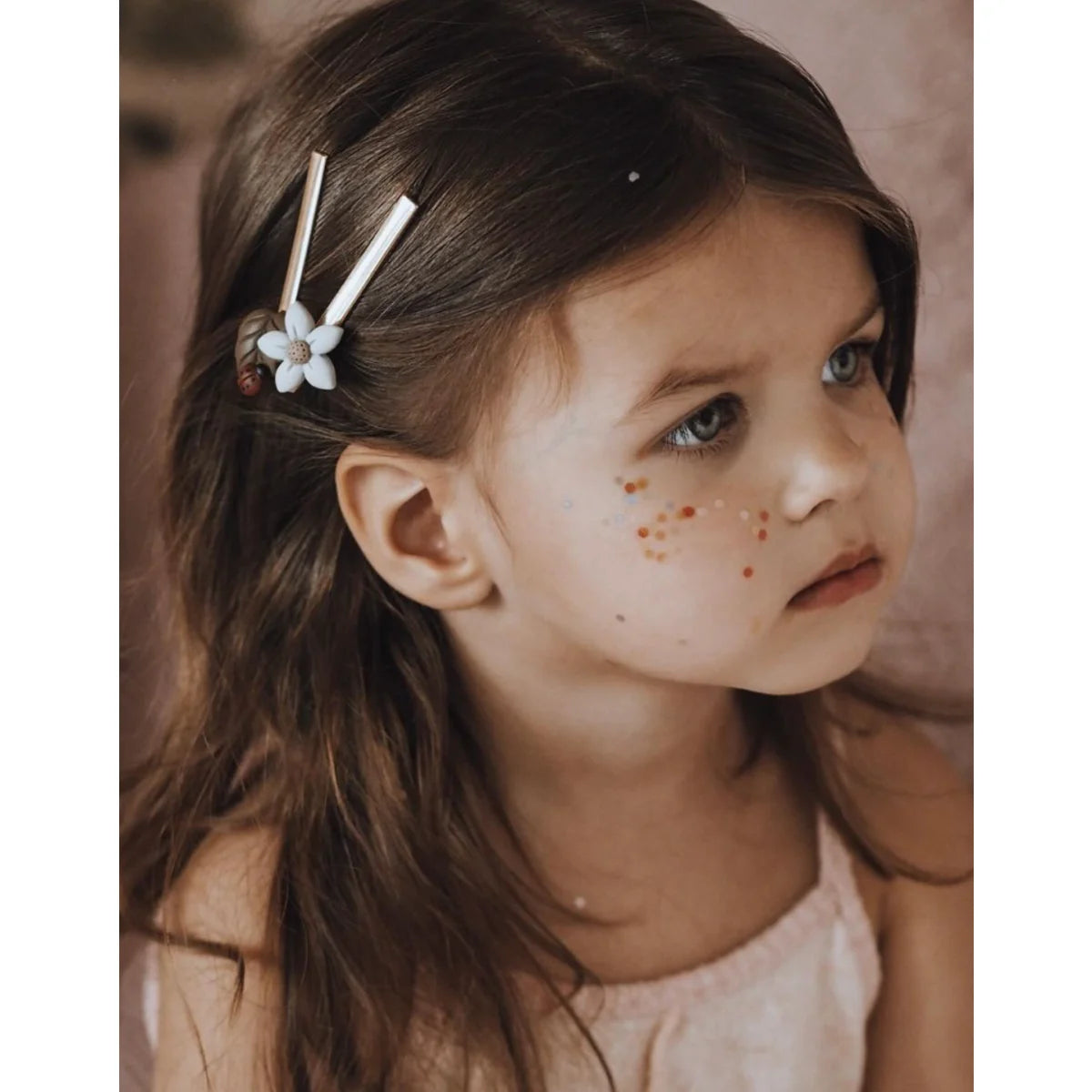 Junges Kind mit dunklen Haaren und Sommersprossen trägt eine weiße Haarspange