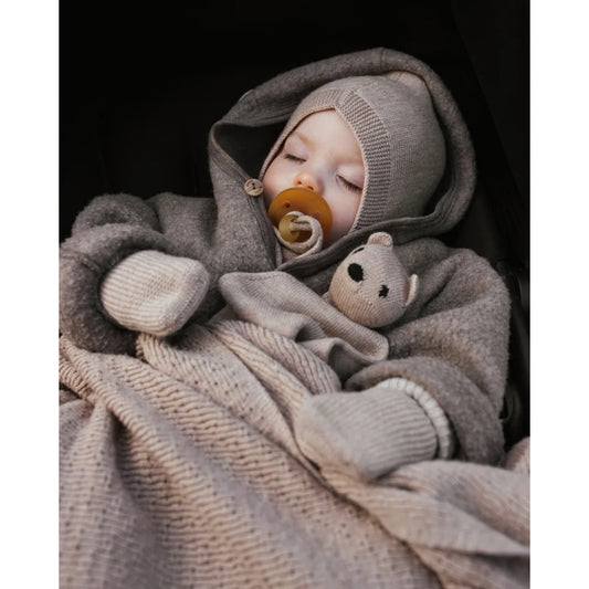 Baby in weichen grauen Strickkleidung und Decken mit Schnuller, Produkt Handschuhe Sand