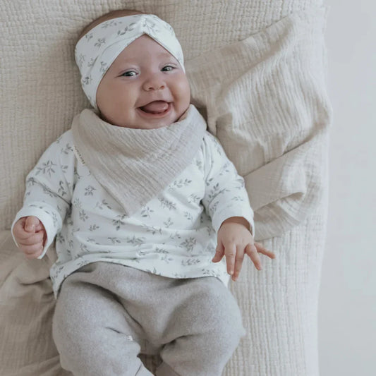 Lächelndes Baby in weißem Outfit und Haarband mit Blättern