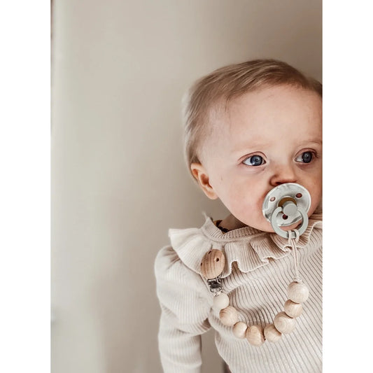 Baby in beiger Ribbstrick-Pulli mit Rüschenkragen und Holz Nuggikette Honey