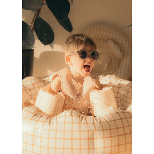 Aufgeregter Kleinkind mit Sonnenbrille und Poolflügeln in einem Inflatable Pool