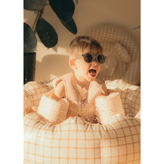 Aufgeregter Kleinkind mit Sonnenbrille und Poolflügeln in einem Inflatable Pool