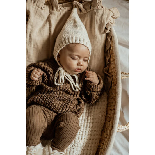 Schlafendes Baby in gestricktem Sweater und Mütze in neutralen Erdtönen
