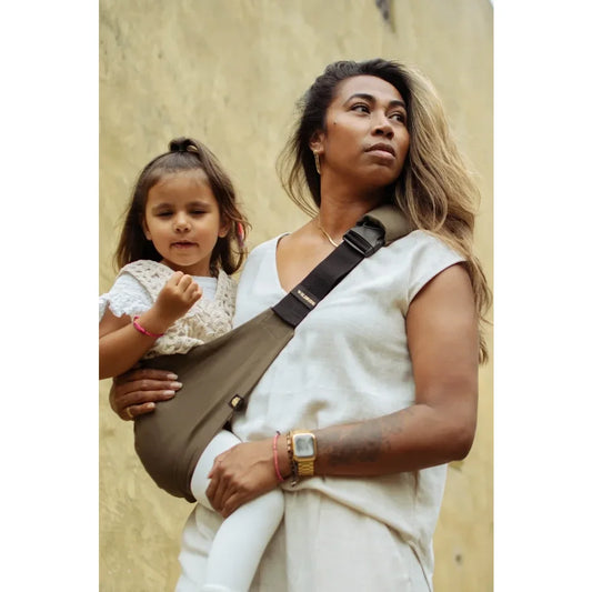 Frau trägt ein Kind in einer Sling-Trage namens Kindertrage | Coffee