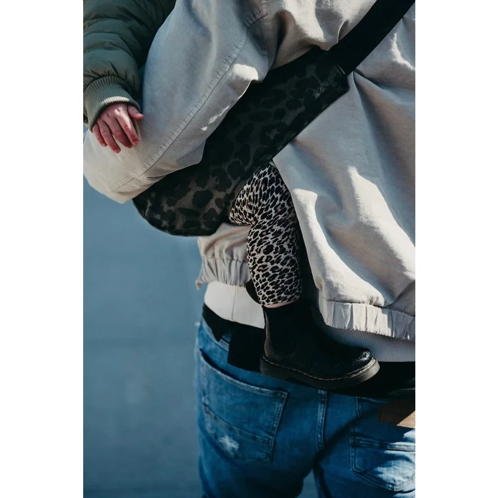 Leopardenmuster-Handtasche mit schwarzem Träger vor weißer Jacke und blauen Jeans