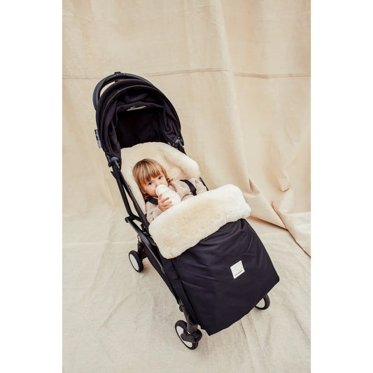 Baby stroller with cozy white and black footmuff featuring a young child inside
