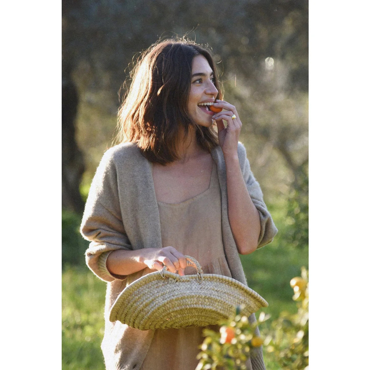 Frau isst eine Orange und hält einen Strohkörbchen, mit Kleid Ava Dress | Rye