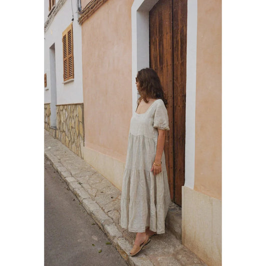 Frau in einem langen, fließenden beigen Kleid steht in einer Türöffnung