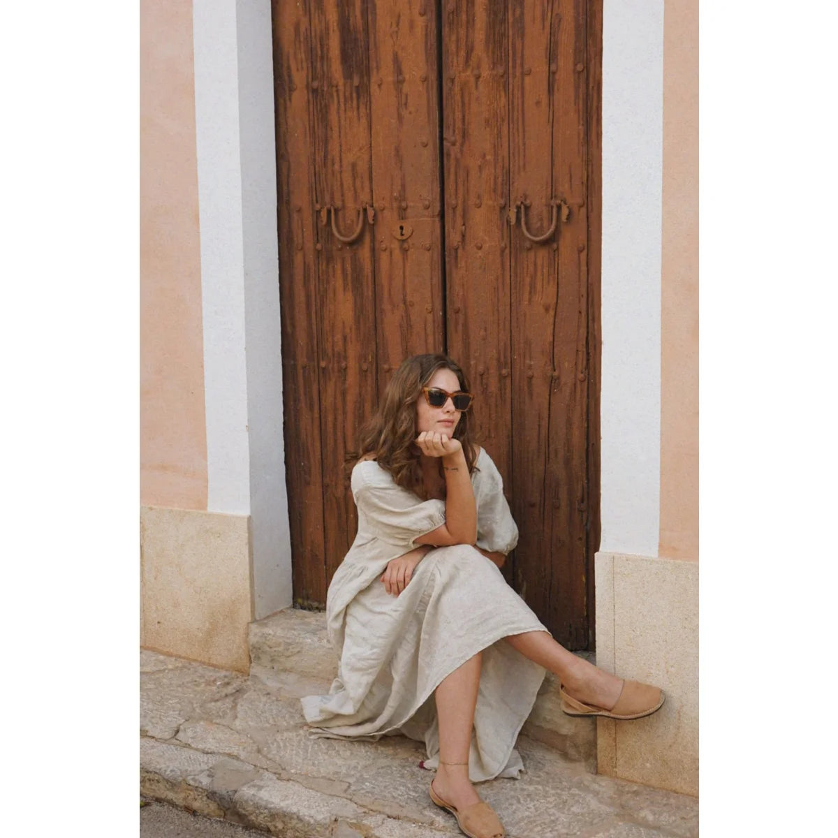 Frau in weißem Kleid sitzt auf Stufen vor einer Holztür, Kleid Paloma von Moon