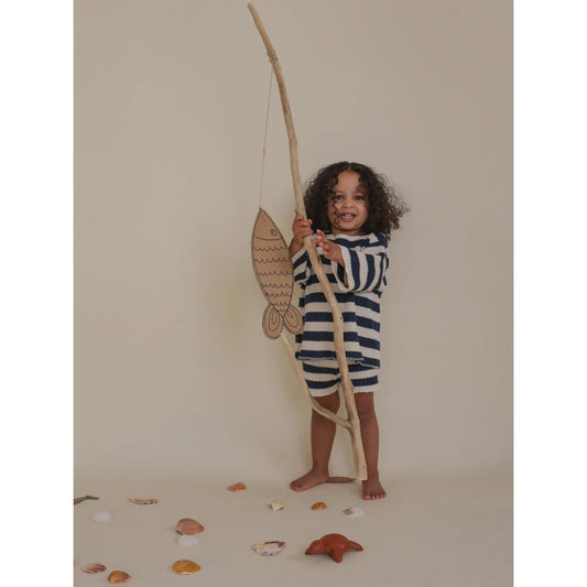 Kind mit Angelrute und Pappfisch trägt gestreifte Strickshorts
