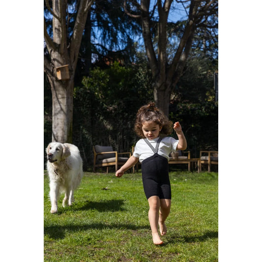 Kind spielt mit Hund in Kurze Strumpfhose mit Träger in klassischem Schwarz-Muster