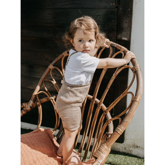 Kind steht in einem gewebten Rattanstuhl mit kurzer Strumpfhose von Peanut Blend