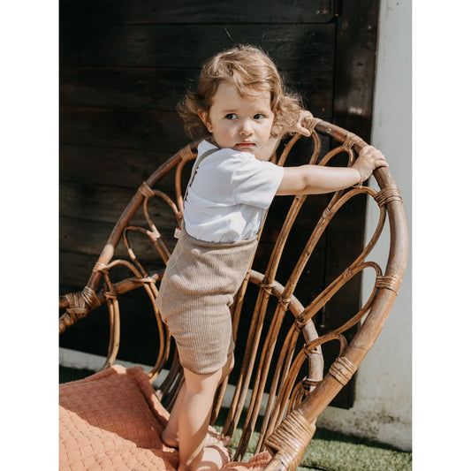 Kind steht in einem gewebten Rattanstuhl mit kurzer Strumpfhose von Peanut Blend