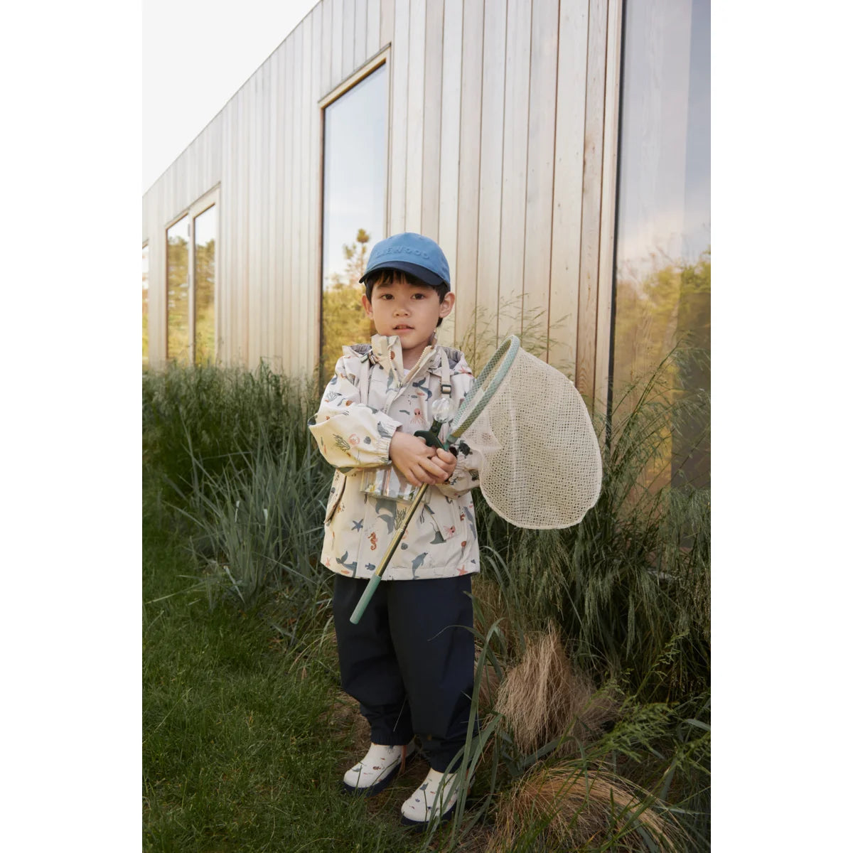 Kind mit Blumenjacke und blauen Mütze hält einen Schmetterlingsnetz