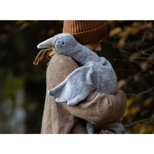 Plüschrabe vor beigem Mantel an einem Kuscheltier Gans gross in grau