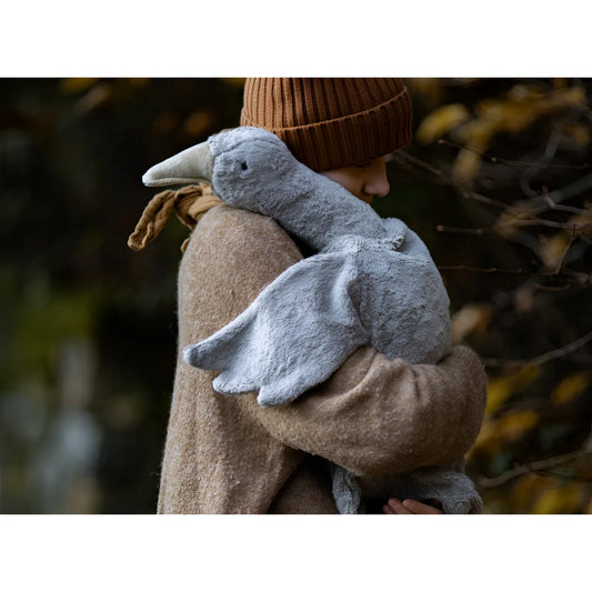 Plüschrabe vor beigem Mantel an einem Kuscheltier Gans gross in grau