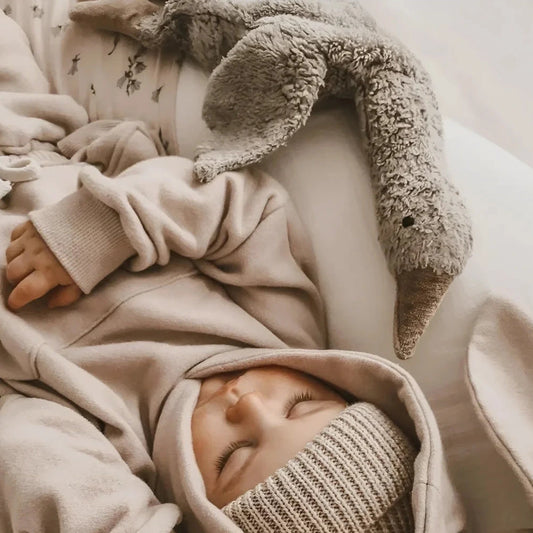 Sleeping baby in neutral blankets with the Senger Naturwelt Cuddly Toy Goose Small in Grey