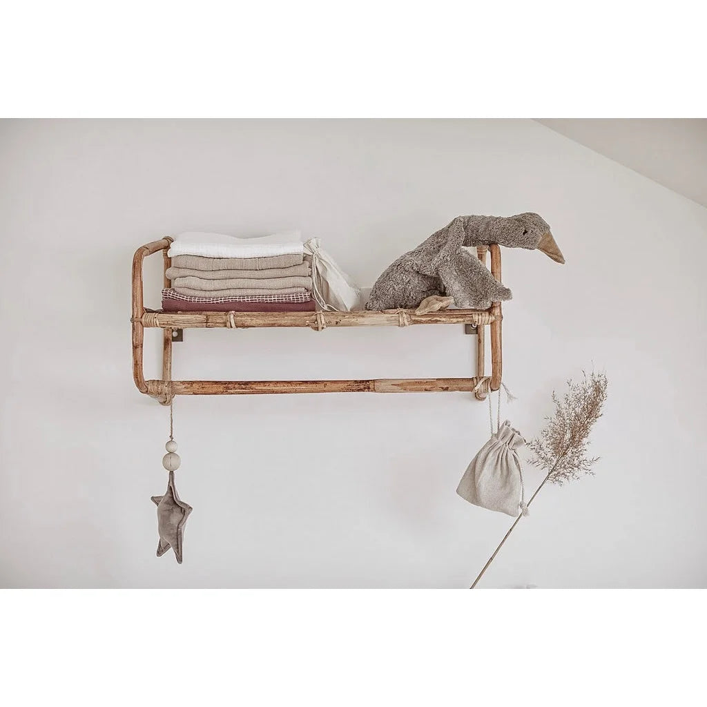 Holzregal mit Kupferrohren, gefalteten Textilien und Kuscheltier Gans klein in grau