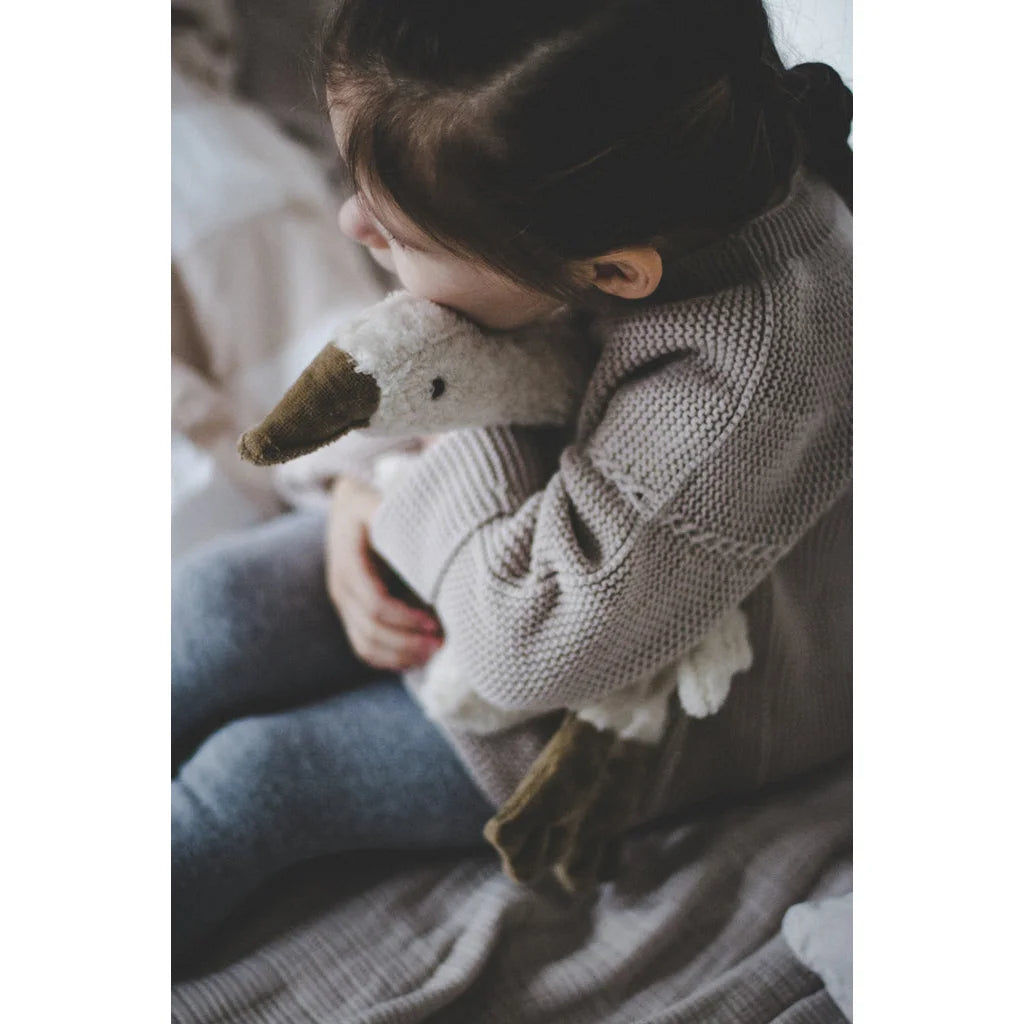 Kind umarmt ein kleines weißes Kuscheltier Gans