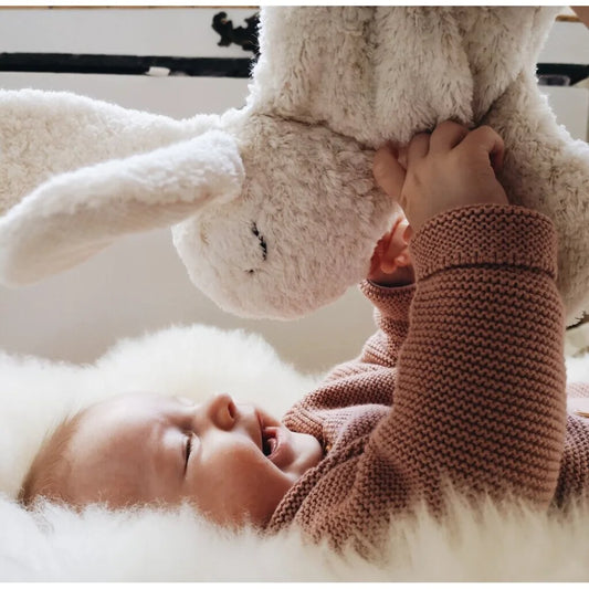 Baby spielt mit einem kleinen weißen Kuscheltier Hase