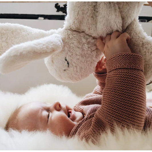 Baby spielt mit einem kleinen weißen Kuscheltier Hase