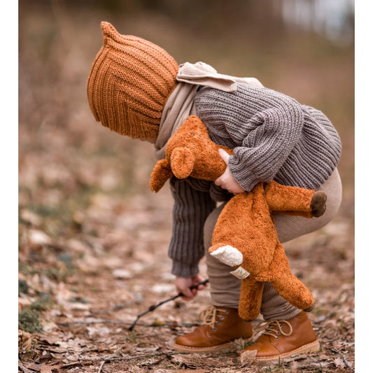 Kind in warmer Winterkleidung umarmt ein Kuscheltier Reh klein