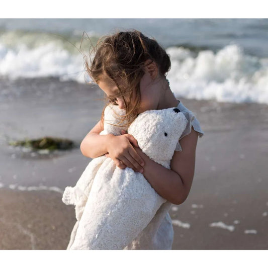 Kind umarmt ein großes weißes Kuscheltier Robbe mit Liebe und Zuneigung