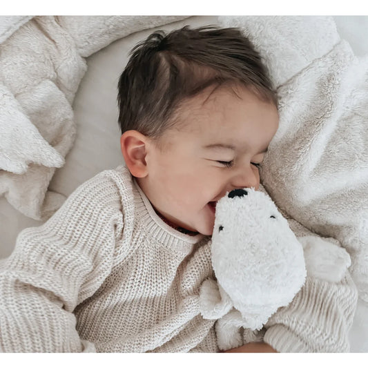 Baby kuschelt mit einem weißen Plüschtier auf dem Bett