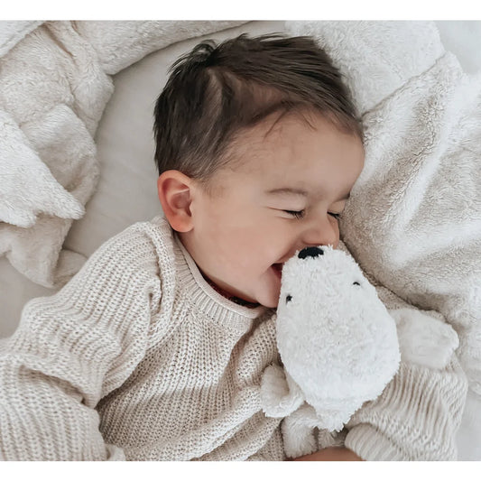 Baby kuschelt mit einem weißen Plüschtier auf dem Bett