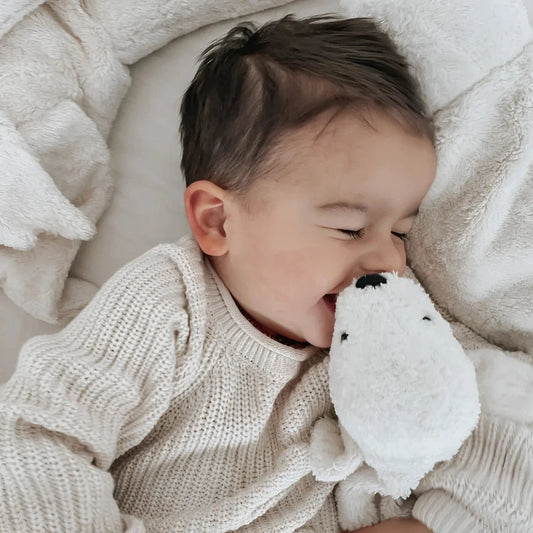 Baby cuddling the white Senger Naturwelt Cuddly Toy Seal Small on the bed