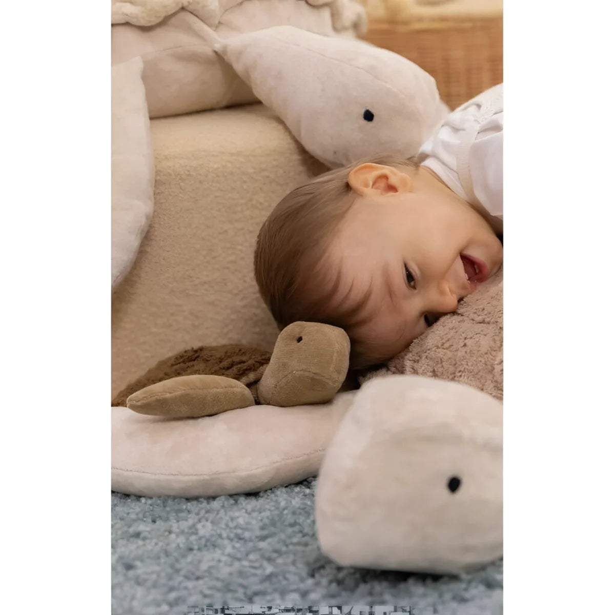 Ein Baby liegt entspannt zwischen weißen Wal-Plüschspielzeugen