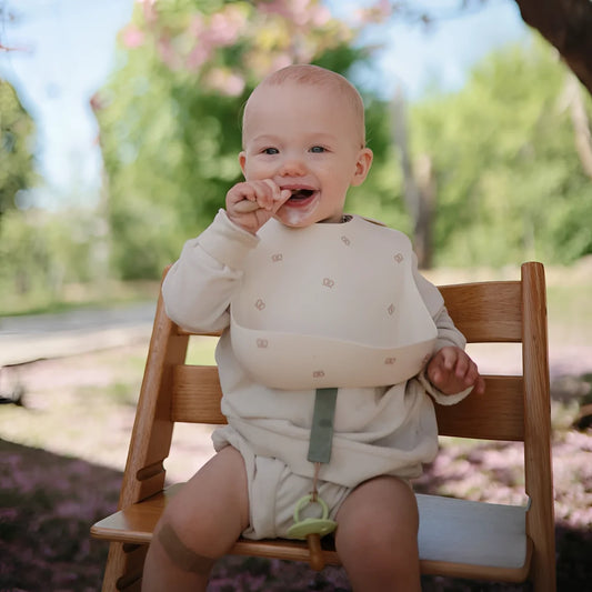 Lächelndes Baby in einem Holzstuhl im Freien mit Lätzchen in Kirschdesign