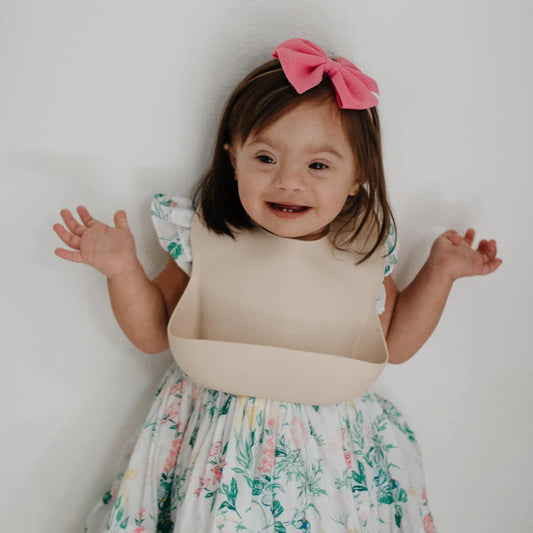 Lächelndes Kind in Blumenkleid und rosa Haarband, passend zum Lätzchen Shifting Sand