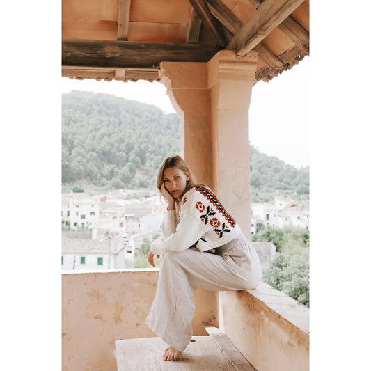 Frau in weißem besticktem Pullover und heller Hose auf Balkon gelockt