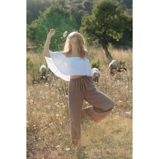 Frau in weißem Crop-Top und braunen Leinenhosen Isla im Grasfeld stehend