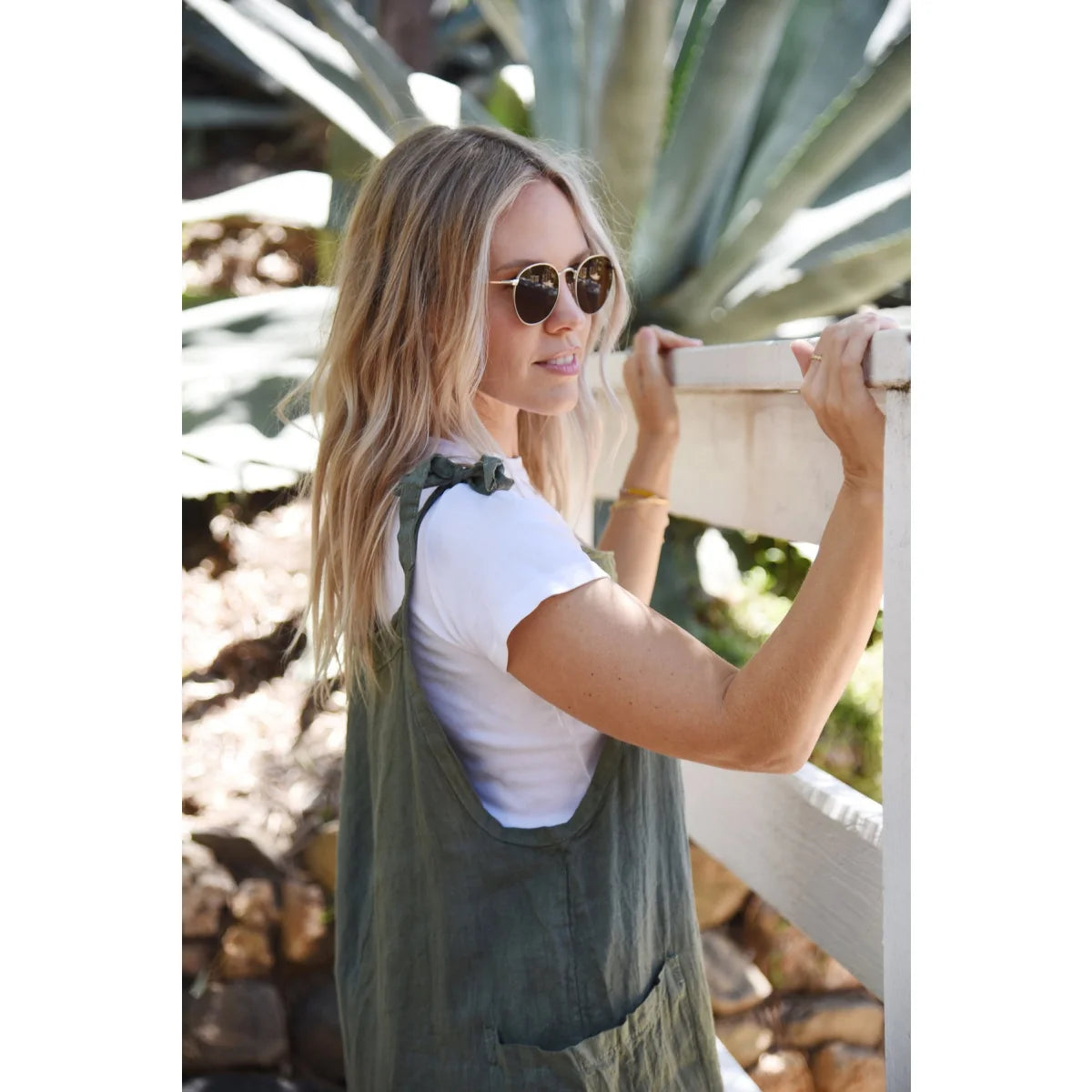 Frau mit langen blonden Haaren in Sonnenbrille und weißem T-Shirt im Leinen Overall Fern