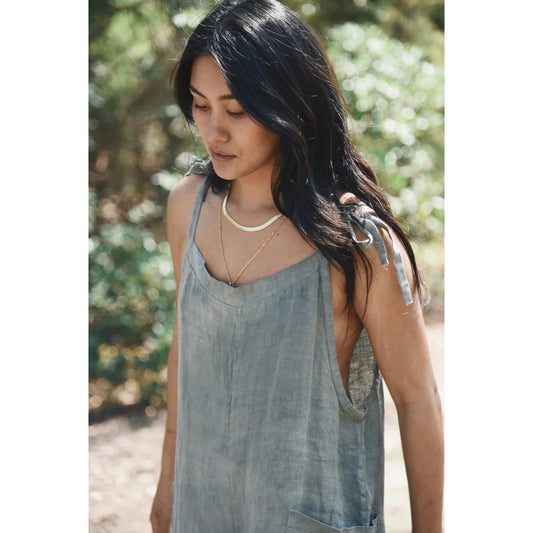 Frau mit langen dunklen Haaren in grauem ärmellosem Top und Perlenkette