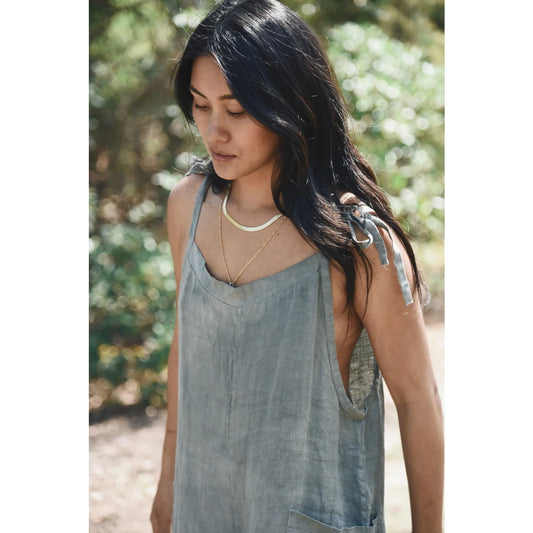 Frau mit langen dunklen Haaren in grauem ärmellosem Top und Perlenkette