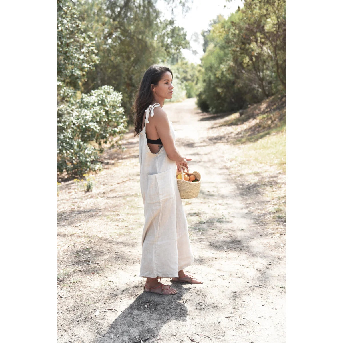 Frau im weißen Sommerkleid auf einem Feldweg mit einem geflochtenen Korb