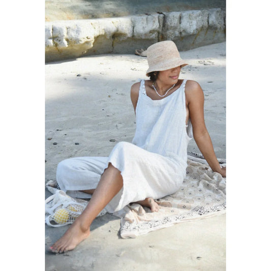 Frau in weißem Outfit und Sonnenhut sitzt am Strand mit Leinen Overall Moon