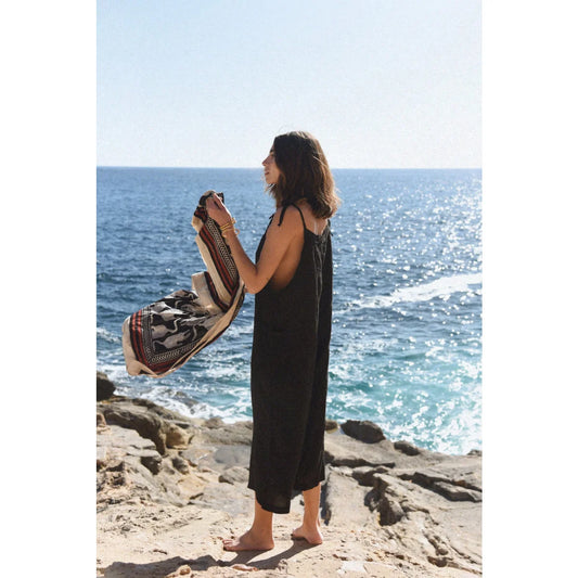 Frau im schwarzen Leinen Overall hält gemusterten Decken, stilvoll und elegant