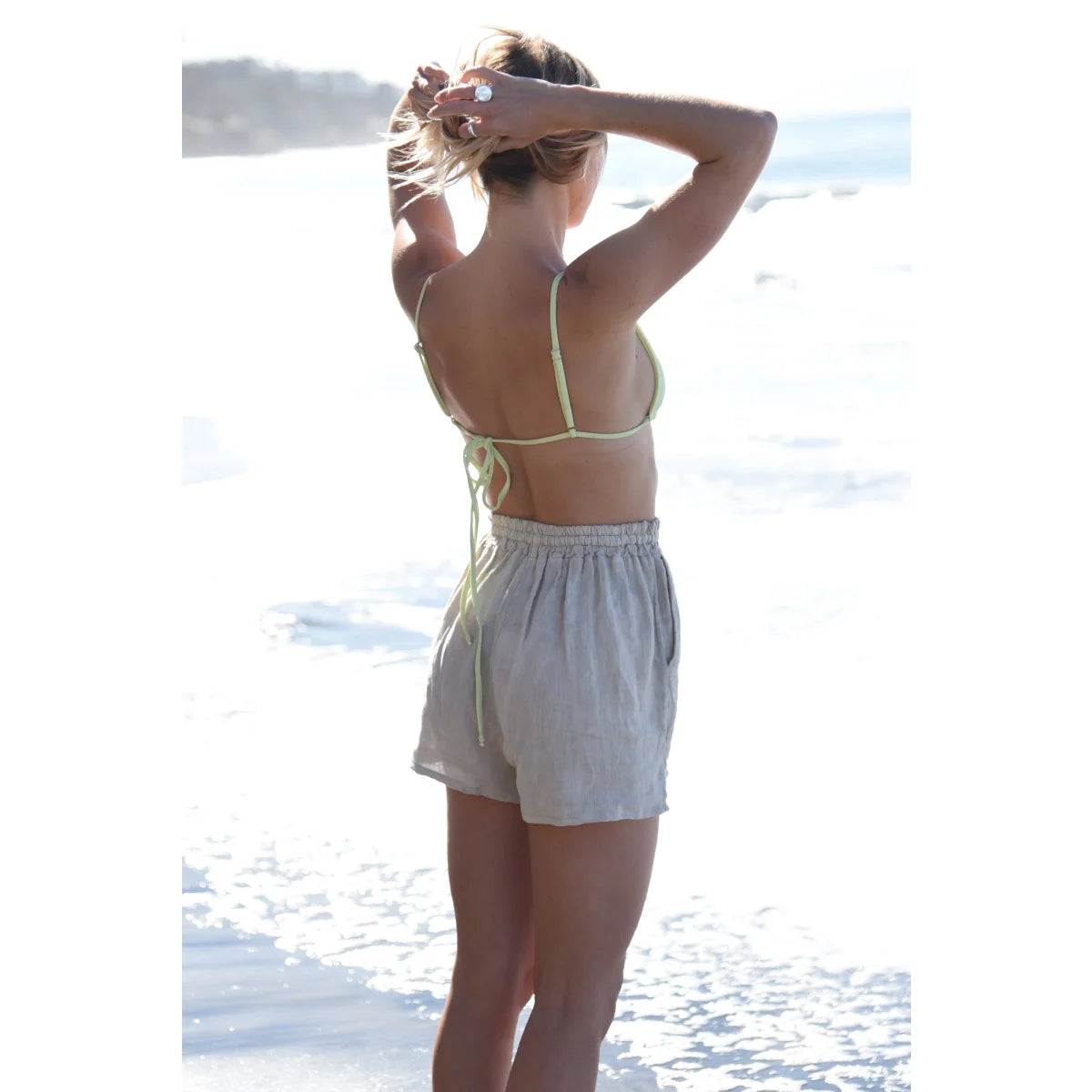 Frau in weißem Oberteil und Shorts am Strand mit erhobenen Händen