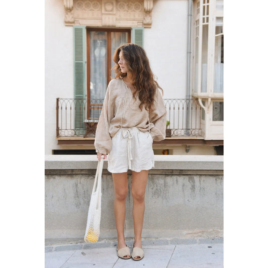 Frau in beigem Pullover und weißen Shorts steht auf einem Bürgersteig mit Leinen Shorts Seashell