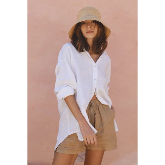 Frau in weißem Hemd, beigen Shorts und cremefarbenem Bucket Hat für Leinen Shorts Seashell