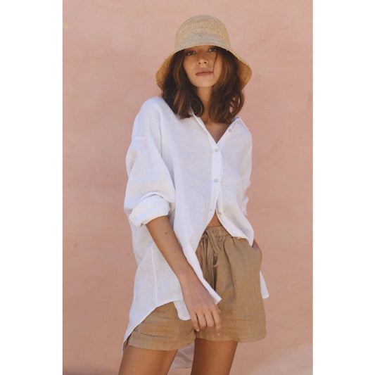 Frau in weißem Hemd, beigen Shorts und cremefarbenem Bucket Hat für Leinen Shorts Seashell