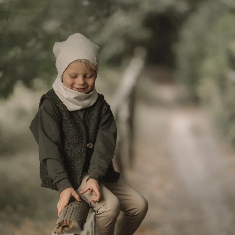 Kinder-Winteroutfit Loop Ecru mit dunkelgrüner Hemd, grauem Weste, beigen Hosen und Mütze
