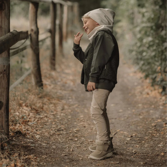 Junges Kind in lockeren hellbeigen Hosen, bequemer Mütze und dunklem Parka