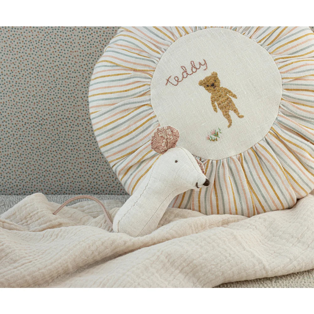 Weißer Plüschschwan neben gestreiftem Kissen mit gesticktem Teddy-Bär-Motiv