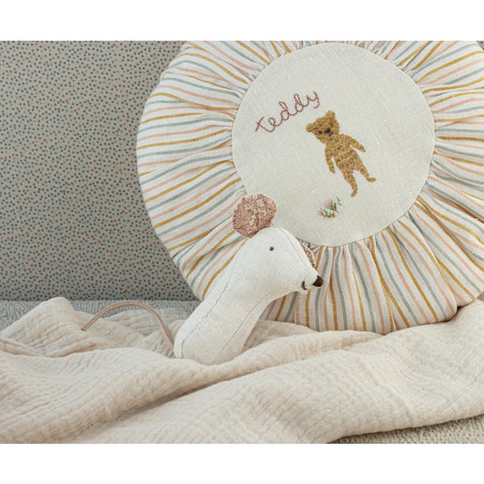 Weißer Plüschschwan neben gestreiftem Kissen mit gesticktem Teddy-Bär-Motiv