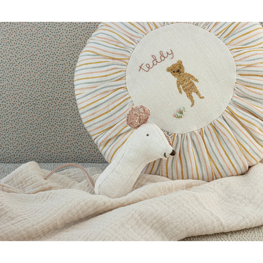 Weißer Plüschschwan neben gestreiftem Kissen mit gesticktem Teddy-Bär-Motiv